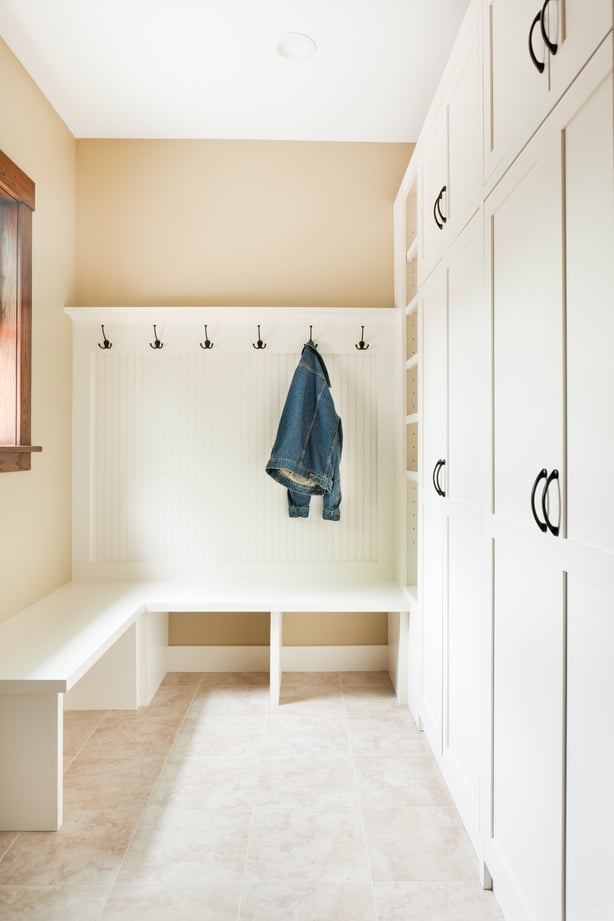 A newly remodeled back door entry way with mudroom with built-in storage painted cabinet closet in white. The room is featuring coat hangers wall, with shoes storage and seating facilities and tile floor. Photographed in vertical format.