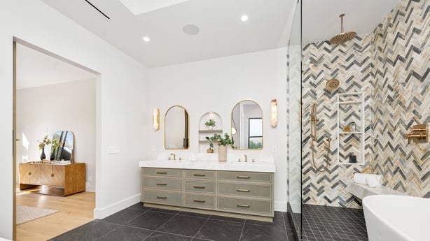 Modern bathroom interior with stylish decor, featuring a double vanity, herringbone tile shower, and sleek black flooring.