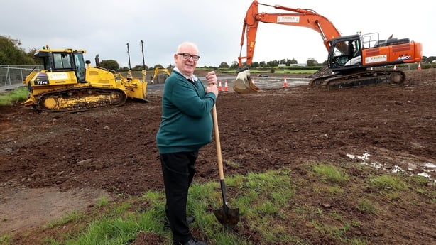 Picture of a man with a shovel in a field with construction vehicles in the background