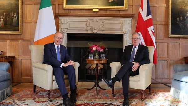 Taoiseach Micheál Martin and UK Prime Minister Keir Starmer sit alongside each other in chairs in front of their respective flags