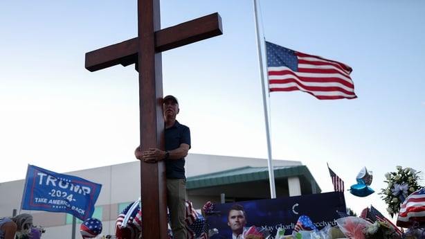 A US flag flies half-staff as a man carries a large cross near a makeshift memorial for Turning Point USA Founder Charlie Kirk