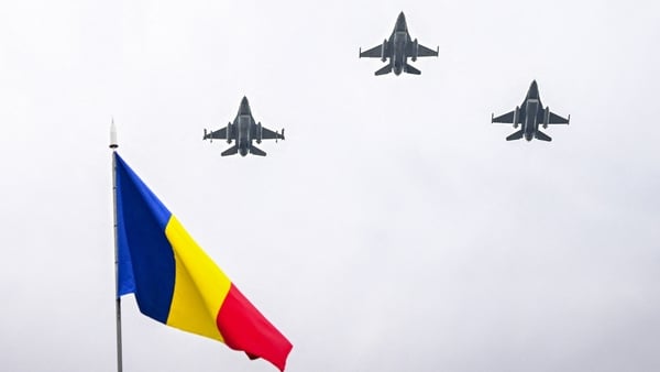 Romanian F-16 jets fly over a Romanian flag during a parade