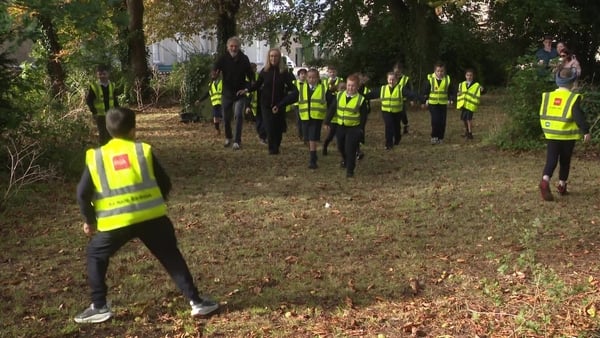 Children wearing hi-vis vests play in a wooded area.