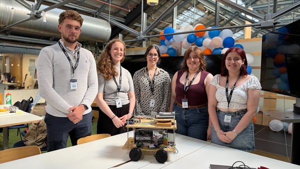 Five young students, four women and one man, stand behind a prototype of an AI-led rover