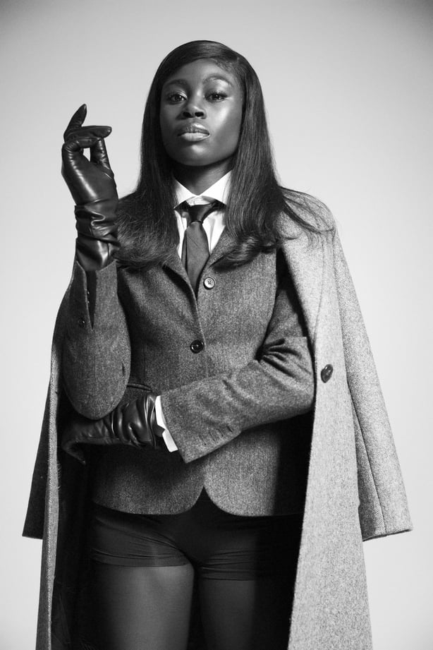 Rhasidat Adeleke wearing Coat €675, TRIONA at trionadesign.comBlazer €350, TRIONA at trionadesign.comShirt €115, Magee 1866 at magee1866.comBlack tie €45, Magee 1866 at magee1866.comGloves, Paula Rowan, stylist's ownShoes, stylist's own