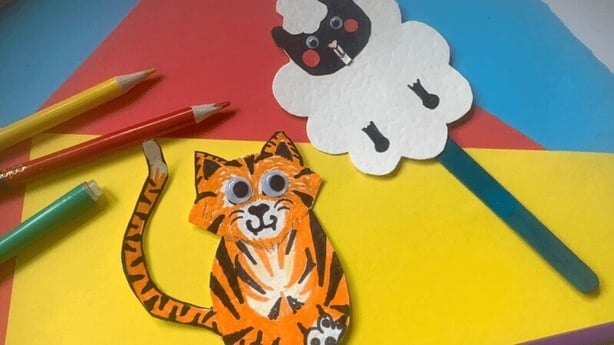Kids artwork on yello, red and blue coloured paper with a cat and sheep stick puppets.