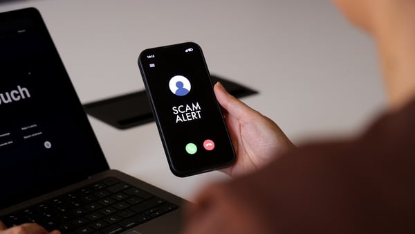 A person holds a smartphone displaying a “Scam Alert” message on an incoming call screen. The dark interface clearly indicates a fraud warning, conveying concerns about cybersecurity, mobile fraud, and digital safety. The indoor environment and close-up c