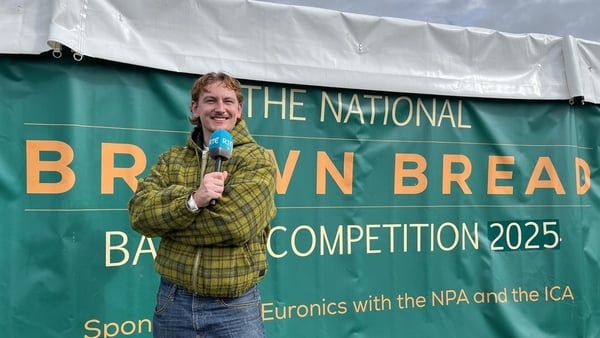 Pj Kirby standing in front of a green sign reading "The National Brown Bread Baking Competition"