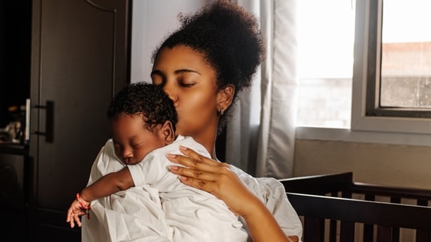 Young adult mother holding and kissing her newborn.
