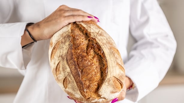 The hands of a young cook are holding freshly baked cereal bread.