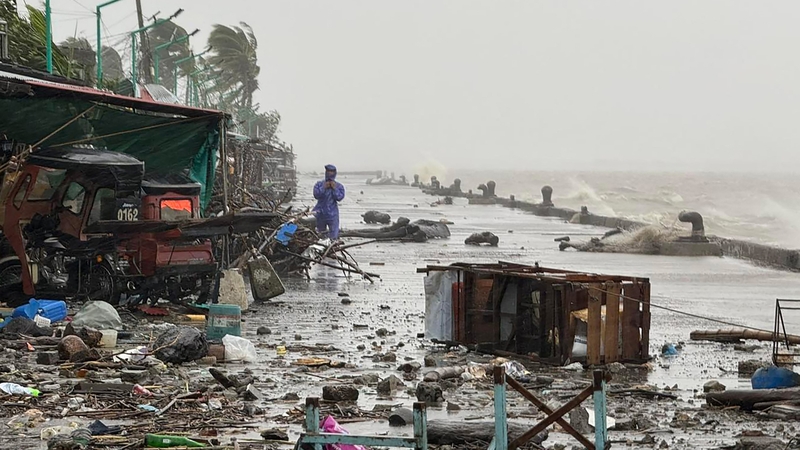A man stands near debris on a waterfront road amid heavy rain due to weather patterns from Super Typhoon Ragasa in Aparri, Philippines