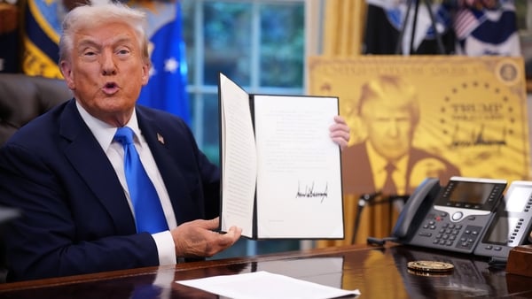 Donald Trump holds up a signed order in the Oval office with an image of his Gold Card behind him