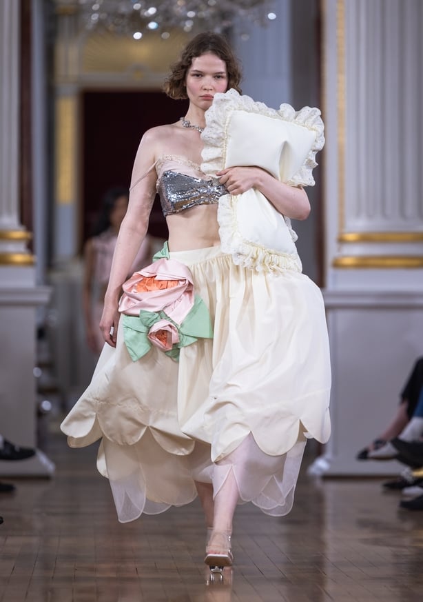 A model wears a silver bra top and a cream skirt with a large floral applique detail on the Simone Rocha runway