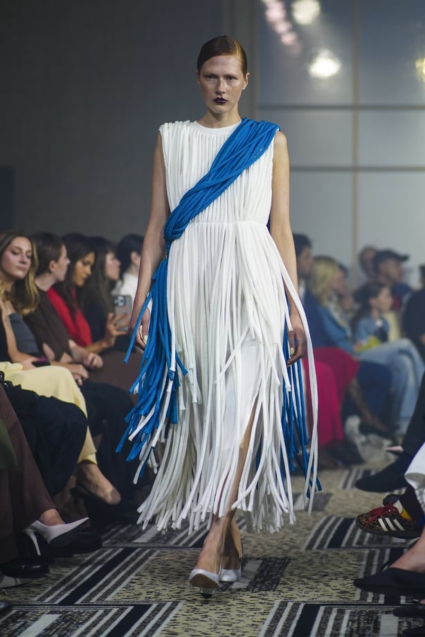 A model wearing a white fringed dress with a blue sash