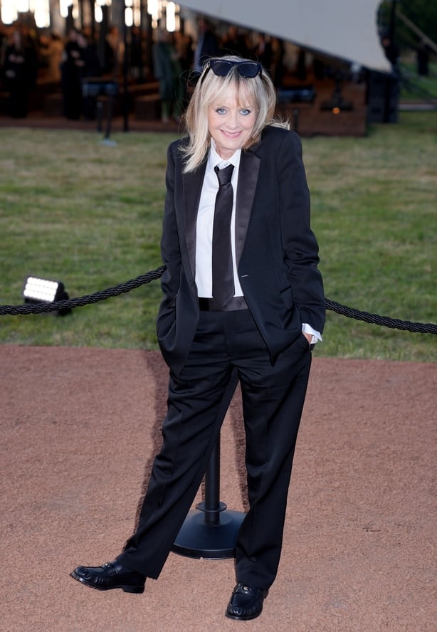 Twiggy wearing a black smoking jacket and black trousers
