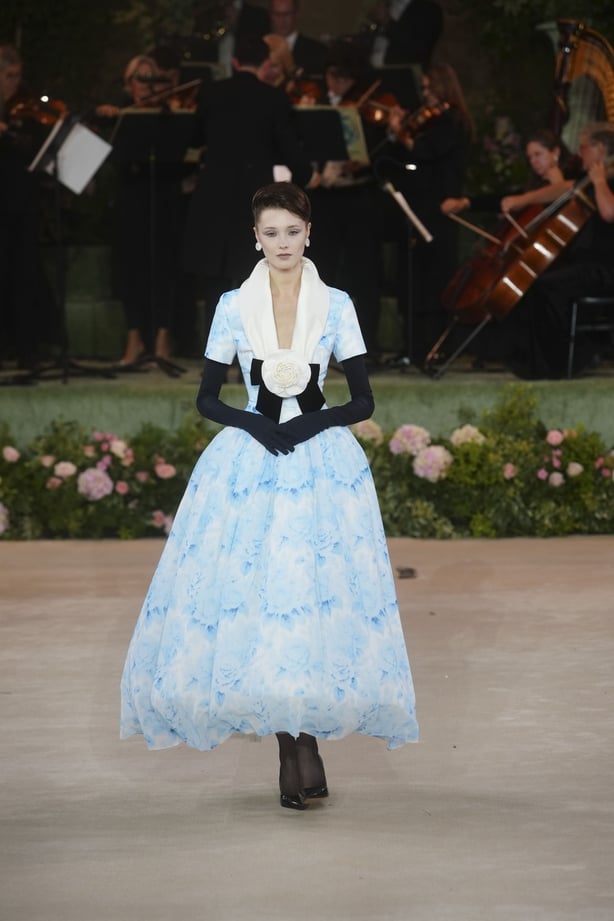 A model wearing a pale blue floral patterned dress with black gloves