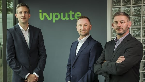 Three men in suits pose for a photo in front of the Inpute company logo