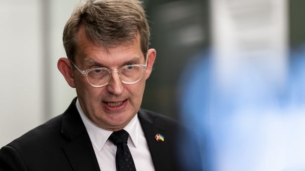 Image shows Denmark's Minister of Defence, Troels Lund Poulsen, wearing a white shirt, black jacket and black tie, with glasses.