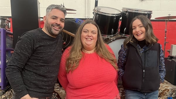 A photo of three people smiling surrounded by musical instruments
