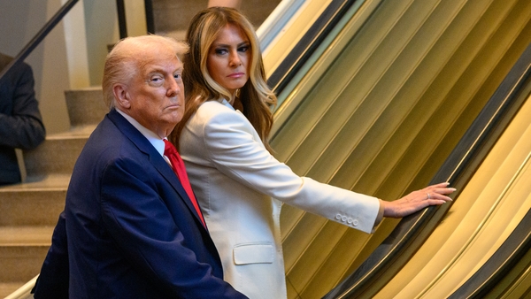 US President Donald Trump and first lady Melania Trump stand at the bottom of an escalator as it refuses to move.