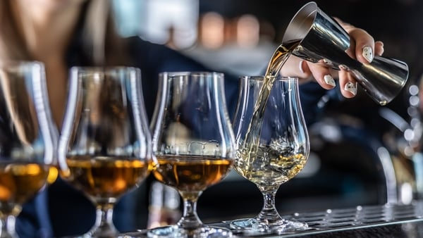Four glasses sit at a table while a person's hand pours liquid into them