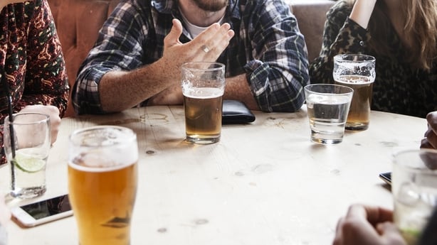 The torsos of a group of men and women can be seen sitting at a table in a pub while drinking beer