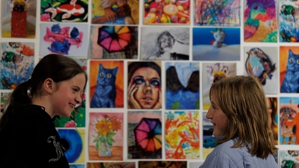 Two girls smiling to each other in front of an art display of postcards.