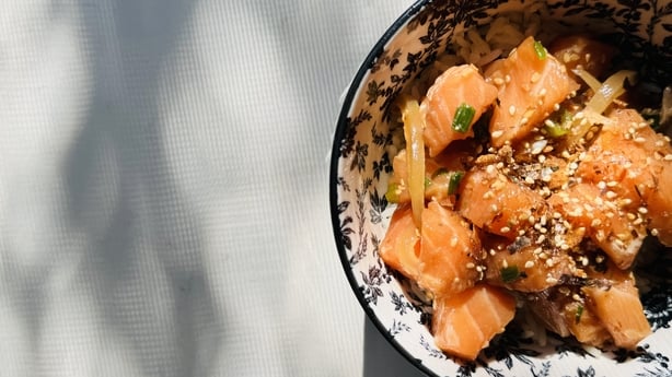 Freshly prepared salmon poke in a bowl resting on a kitchen counter with sunlight and shadows streaming in through the window.