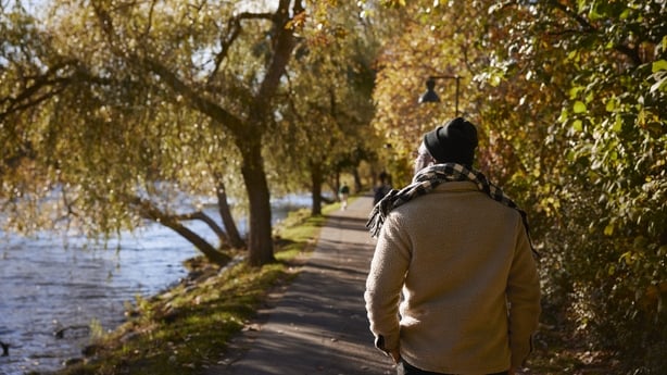 An older man walking along a river and autumnal trees