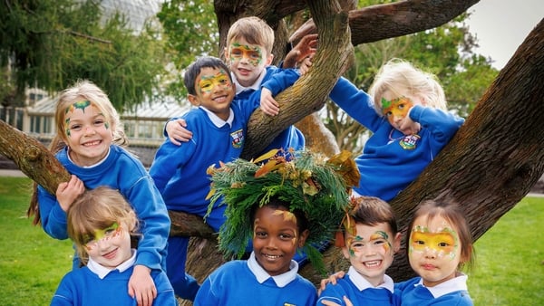 School children in blue uniforms pose in a tree with face paint and fun decorations.