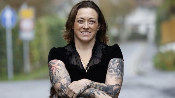 A woman with brown hair, wearing a black shirt smiles to the camera