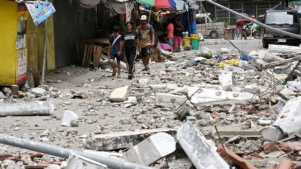 Residents walk past rubble in Bogo City on October 1, 2025, after a 6.9-magnitude quake struck off the coast of the central Philippines