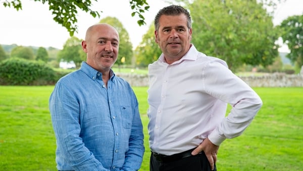 Two men pose for a picture in a field