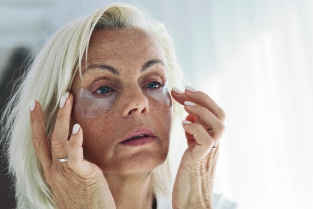 Older woman applying on her face hydrogel under-eye recovery patches. 