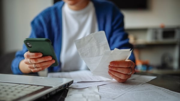 middle-aged woman with glasses, laptop, smartphone, and papers at a table at home
