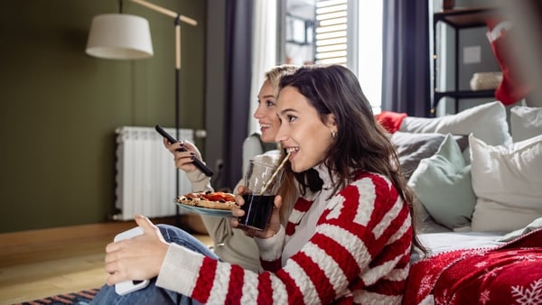 Two young woman watching TV at home. They are eating pizza and relaxing. From Getty Images RTE