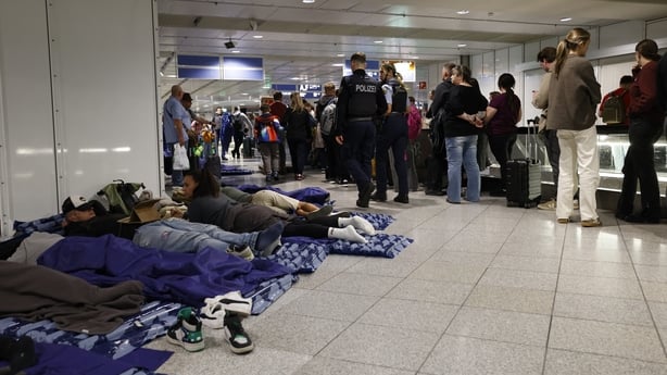 Passengers sleep on inflatable mattresses on the ground while others queue up next to them at Munich International Airport