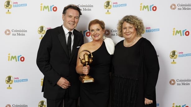 Michael O'Kane, Sinéad Wylde and Gail Henry stand together beside each other holding a gold trophy