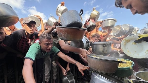 Palestinians wait with their empty pots to receive hot meals distributed by charity organizations in the al-Mawasi area