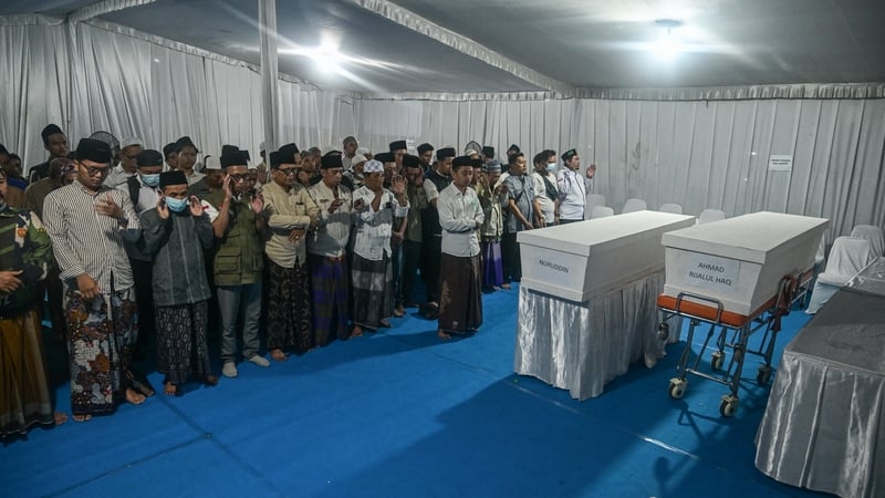 People and family members pray for a student killed in the building collapse in Indonesia