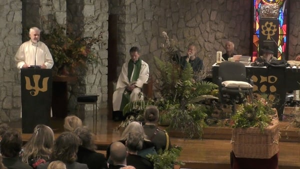 A view from inside the chapel during Manchán Magan's funeral. A priest speaks at the alter while the coffin lies in state to his right.