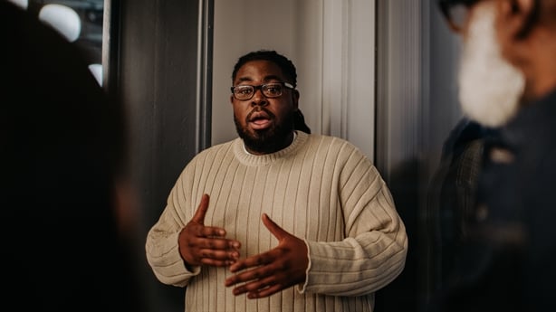 A man has a serious expression as he talks to onlookers. He uses his hands to gesture as he explains and discusses a matter with his coworkers / audience.