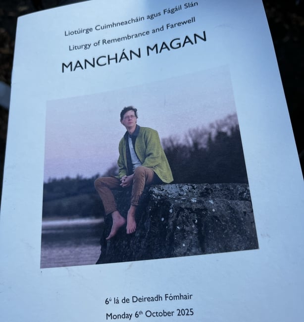 A leaflet of white paper shows a picture of a man in a green jacket sitting on a rock with a body of water in the background.