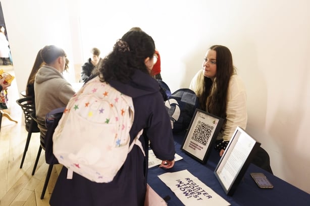 A secondary school student speaking to another woman at a table