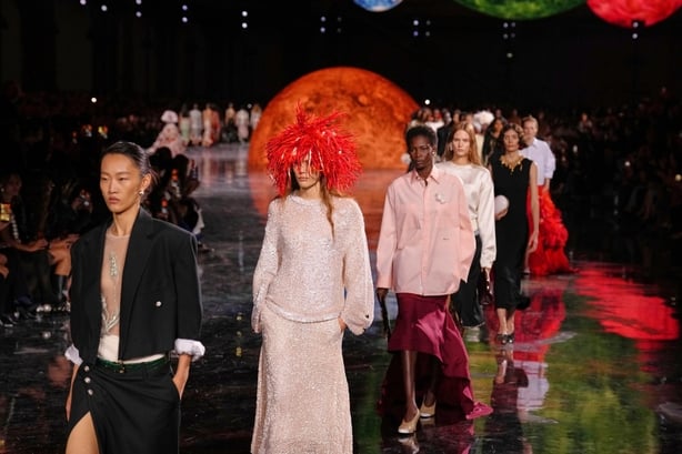 Models walk the runway at Chanel's fashion show, with a mirrored runway and large planet-shaped installations