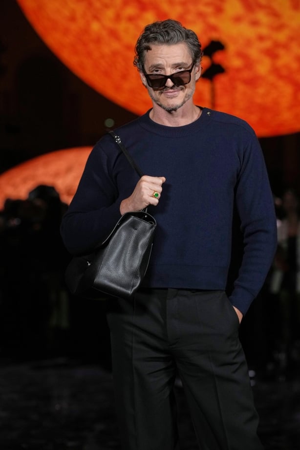 Pedro Pascal poses for a photo in front of a large globe shaped like the sun