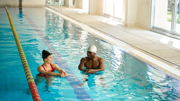 Woman in red swimsuit standing near male and talking, coach conducting swimming lesson