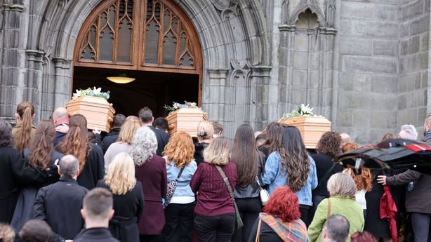 People gather as three coffins are carried into a church 