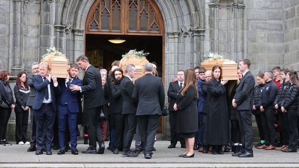 Mourners carrying three coffins outside church
