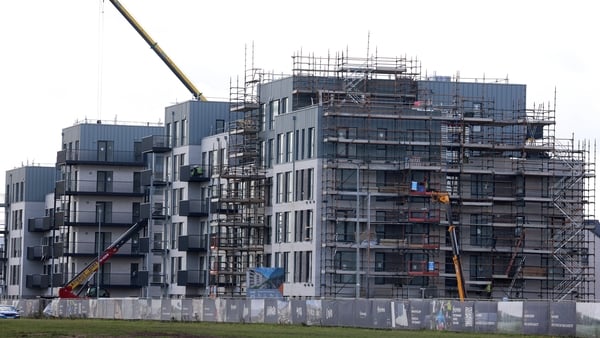 A yellow crane looming over an almost complete apartment building site surrounded by scaffolding